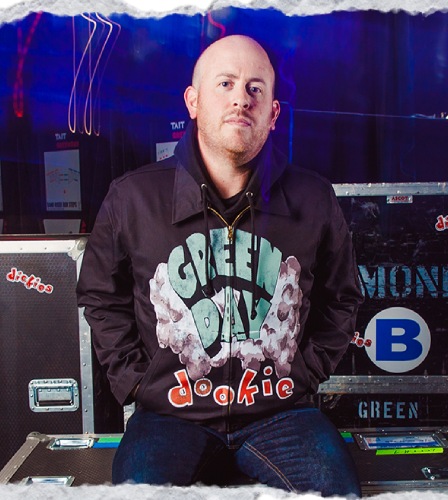A black jacket with a brass zipper featuring the classic 'Green Day Dookie' logo on the front, where Green Day is written in green sitting on top of the bomb cloud and featuring red dookie writing below. A small Dickies logo sits on the bottom right next to slash front welt pockets.